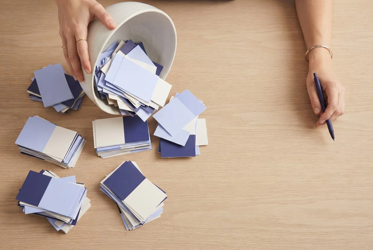 Colour-block cards poured from a bowl land in uneven piles of different sizes on a table.